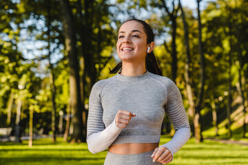 Smiling young woman is jogging and listening to the music in a green park