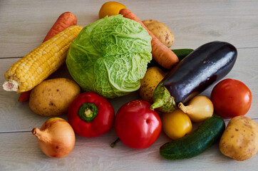 Composition with assorted raw organic vegetables on white wooden background. Potatoes, cucumber, onion, eggplant, cabbage, carrots, corn, tomato, pepper in a chaotic manner.