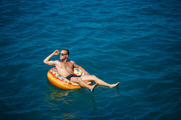A young man swims in the open sea on an inflatable ring on a sunny day. Summer vacation, tourist on...
