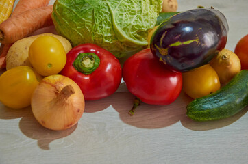 Composition with assorted raw organic vegetables on white wooden background. Potatoes, cucumber, onion, eggplant, cabbage, carrots, corn, tomato, pepper in a chaotic manner.