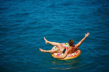Obraz na płótnie Canvas A young man swims in the open sea on an inflatable ring on a sunny day. Summer vacation, tourist on vacation