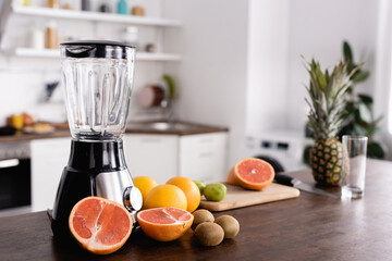 Selective focus of ripe fruits near blender on kitchen table