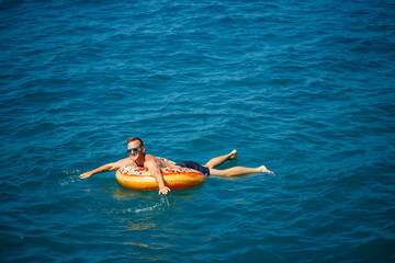 a man lies on a large inflatable rubber circle and floats on the blue sea on a bright sunny summer day