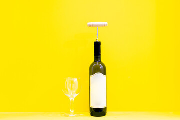 white wine bottle with opener in cork ad empty glass isolated in yellow blank space background