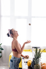 Selective focus of young housewife throwing kiwi near cutting board and blender
