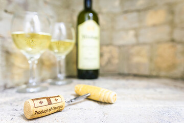wine opener with cork in focus with blurry background of gerogian white wine bottle and two full...