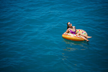 Carefree young girl woman enjoying a relaxing day at sea, floating on an inflatable ring, top view. Sea vacation concept