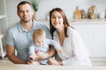 Happy cheerful young family together with infant baby girl in kitchen at home