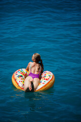 Beautiful young woman in the sea swims on an inflatable ring and has fun on vacation. Girl in a bright swimsuit at the sea under the sunlight