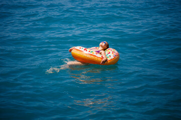 Beautiful young woman in the sea swims on an inflatable ring and has fun on vacation. Girl in a bright swimsuit at the sea under the sunlight