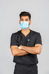 indian doctor or surgeon in black uniform with stethoscope and white latex gloves, blue medical mask on gray background