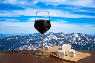 Glass of red wine against mountains background. Closeup view of glass of red wine over snowy...