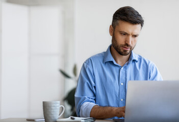 Concentrated businessman working on laptop at workplace in office, typing on keyboard