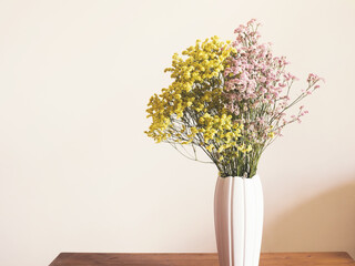 Dried pink and yellow flowers in white vase against white wall. Home interior autumn decor. Copy space