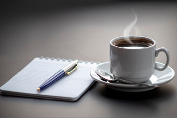 A cup of coffee with steam on the table. Planning and starting the day.