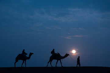 Man and a camel walking across sand dunes in Jaisalmer, Rajasthan, India.