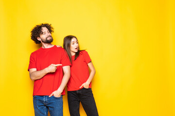 Young couple pointing to the side to present a product isolated on yellow background