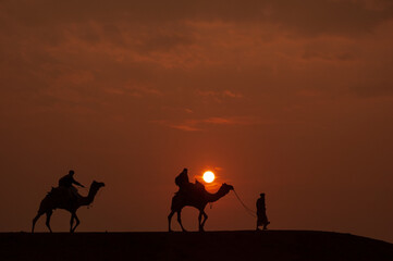 Man and a camel walking across sand dunes in Jaisalmer, Rajasthan, India.