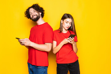 Obraz premium Photo of excited people man and woman holding smartphones in hands isolated over yellow background