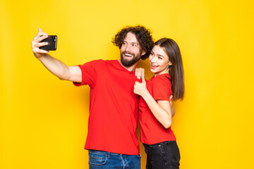 Young lovely couple posing together while making selfie on smartphone isolated over yellow background