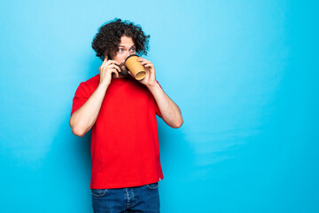 Young handsome man holding coffee to take away and talk mobile phone over isolated blue background