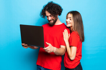 Obraz na płótnie Canvas Portrait of a two happy young men and woman holding laptop computer isolated over blue background.