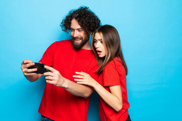Happy young couple look at mobile phone on blue background