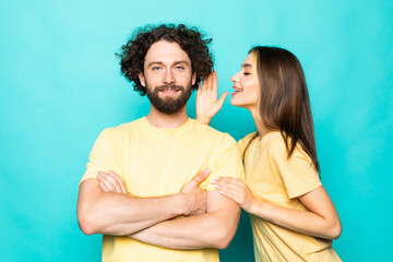 Young couple is listening gossip in the ear each other on the turqouise background.