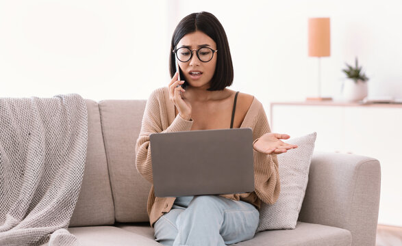 Frustrated Asian Woman Talking On Mobile Phone Sitting On Sofa