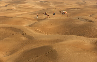 Fototapeta na wymiar Man with camel walking across sand dunes in Jaisalmer, Rajasthan, India.
