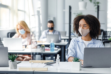 Obraz premium Work on project in corporate company after lockdown. African american woman in mask creating idea at workplace with smartphone and protective glass