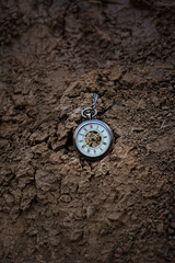Fototapeta na wymiar vintage pocket watch on dark rough earth background. concept of past or future tense. time and earth. copy space