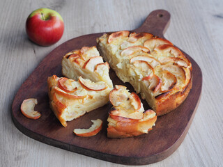 Slices of homemade apple pie on a wooden kitchen board and fresh apple on the table, closeup. Traditional delicious dessert baked goods with seasonal natural fruits