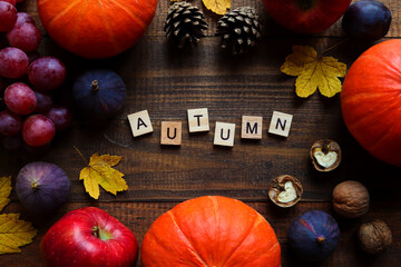 Autumn composition with seasonal products and inscription AUTUMN made from wooden letters.Pumpkins, grapes, figs, apples, pine cones, walnuts, and maple leaves. Autumn mood postcard.Top view, flat lay