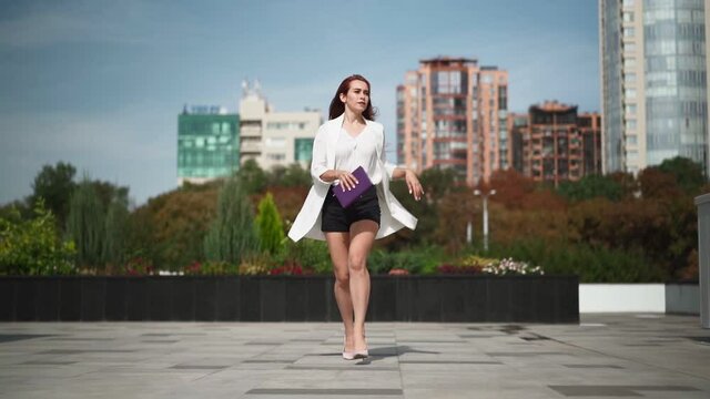 Beautiful business woman with a phone and a notebook in her hands is late and runs in heels to work through downtown. Woman student rushes to the couple at the university. Slow motion