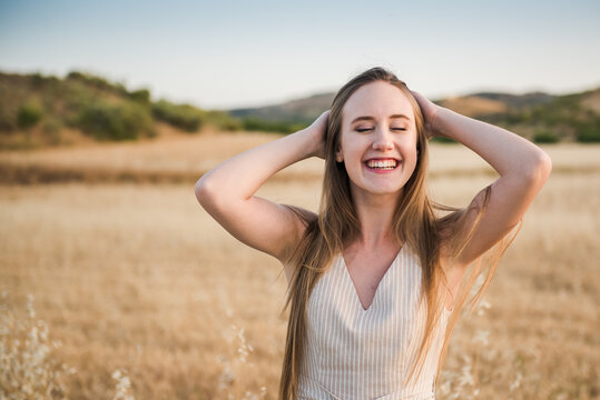 Beautiful blonde woman laughing with her hands on her head and her eyes closed. Long haired caucasian girl happy on a field