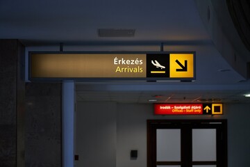 Arrivals hall sign at an airport with dim light and no people. The first line in Hungarian language...