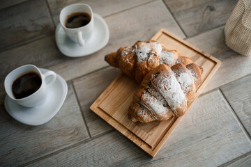 Fresh pastries croissants with chocolate on a wooden board and two cups of black coffee. Romantic breakfast