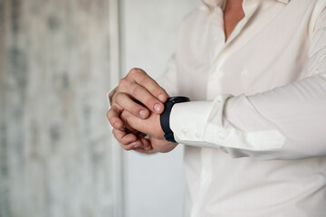 Obraz na płótnie Canvas A man elegant businessman buttons a watch on his hand he is dressed in a white dress shirt