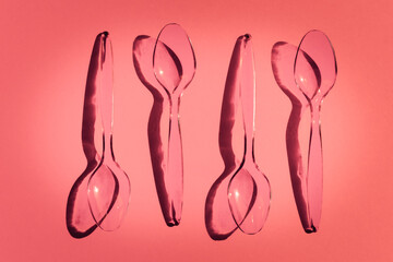 Disposable plastic spoons on pink background with contrasting shadows