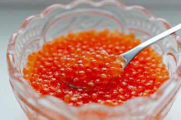 Red caviar in a transparent crystal plate, in a plate is a metal spoon
