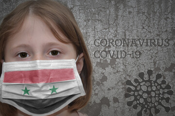 Little girl in medical mask with flag of syria stands near the old vintage wall with text...