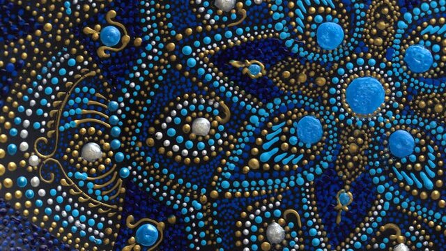 Decorative ceramic plate with black, blue and golden colors, painted plate rotating on background, closeup, top view. Decorative porcelain plate painted with acrylic paints, handwork, dot painting