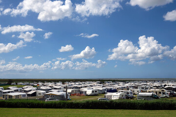 Fototapeta premium Weiter Blick über Campingplatz bei Dornumersiel an der Nordseeküste auf die ostfriesischen Inseln Baltrum und Norderney am Horizont bei sonnigem Wetter mit blauem Himmel und weißen Wolken - Stockfoto