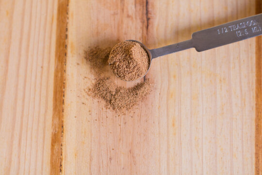 Nutmeg powder in measuring spoon close up with wooden neutral background