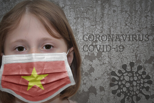 Little girl in medical mask with flag of vietnam stands near the old vintage wall with text coronavirus, covid, and virus picture. Stop virus concept