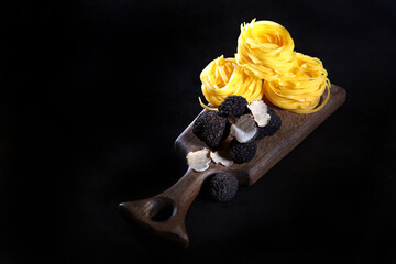 Black truffles and pasta in the form of nests on a wooden Board. Black background.Top view.