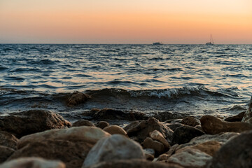 The sun goes into the sea or ocean at sunset, photographed from under the rocks on the shore