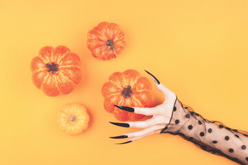 Witch hands with long black nails are holding a pumpkin on the orange background. Halloween...