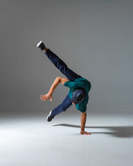 Cool b-boy dancing on one hand in studio isolated on gray background. Breakdance poster